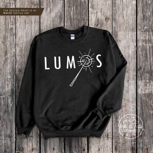 May include: Black sweatshirt with a white graphic of a wand and the word "LUMOS" on the front.