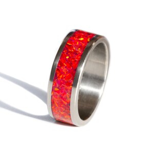 Può includere: Un anello d'argento con un'incisione di opale rosso. L'anello è largo e ha una finitura lucida.