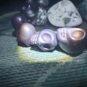May include: A bracelet made of black and gray skull beads, a green and white agate stone, and other dark beads.