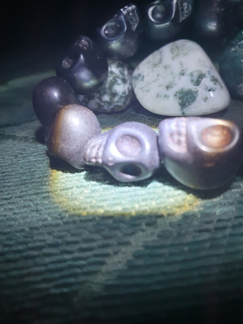 May include: A bracelet made of black and gray skull beads, a green and white agate stone, and other dark beads.