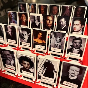 Peut inclure: Un plateau de jeu avec des cartes blanches repr&eacute;sentant des personnages de films d'horreur. Les cartes sont dispos&eacute;es en rang&eacute;es et en colonnes, et chaque carte contient une image d'un personnage et son nom. Parmi les personnages, on trouve Gomez, Edward, Nosferatu, Edgar, Dracula, Lily, Mary, Elizabeth, David, et bien d'autres.