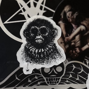 May include: Black and white line drawing of a monkey's face with a detailed, textured fur pattern. The drawing is on a white sticker.