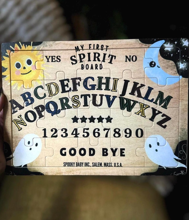 Pu&ograve; includere: Un tabellone di puzzle in legno con la scritta "MY FIRST SPIRIT BOARD". Il tabellone presenta lettere, numeri e le parole "YES", "NO" e "GOOD BYE". Ha illustrazioni di sole, luna e fantasmi.