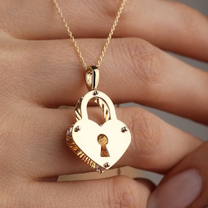May include: A gold heart-shaped padlock necklace with a keyhole. The pendant is detailed with a textured design and small accents.
