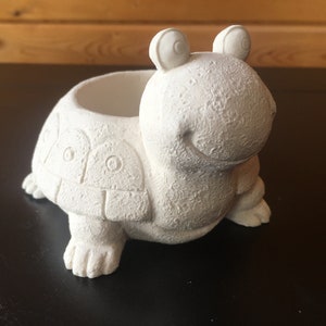 May include: White ceramic turtle planter with a small pot on its back. The turtle has a smiling face and large eyes.