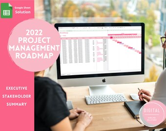 May include: A computer screen shows a 2022 project management roadmap, with a spreadsheet layout. The image includes the text "2022 Project Management Roadmap" and "Executive Stakeholder Summary". A person is sitting at a desk with a keyboard and notebook.