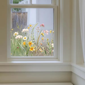 Könnte beinhalten: Ein Fenster mit einem floralen Aufkleber mit Wildblumen im Aquarellstil in Gelb-, Weiß- und Rosatönen. Der Aufkleber ist auf dem unteren Teil des Fensters angebracht und bildet einen dekorativen Rand. Das Fenster ist weiß gerahmt.