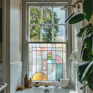 May include: A bathroom window with a stained glass design. The window features a geometric pattern with rectangular and semi-circular shapes in pastel colours. The top portion of the window offers a view of trees and the sky.