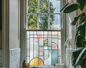 May include: A bathroom window with a stained glass design. The window features a geometric pattern with rectangular and semi-circular shapes in pastel colors. The top portion of the window offers a view of trees and the sky.