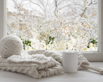 May include: A white ceramic mug sits on a white surface next to a ball of white yarn and a knitted sweater. The background is a window with a snowy scene and a floral design.