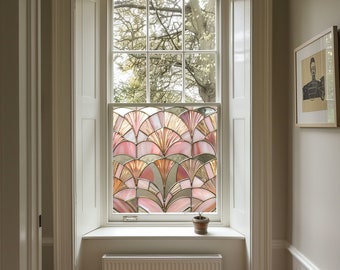 May include: A window with a decorative stained glass film featuring a fan-shaped design in shades of pink, peach, and gold. The window is set in a white frame within a light-colored room. A small potted plant sits on the windowsill.