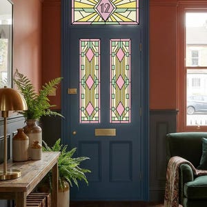 May include: A dark blue front door featuring stained glass panels with a geometric pattern in yellow, pink, and green. The transom window above the door displays the number 12 in a central diamond shape, complemented by a brass letter plate.