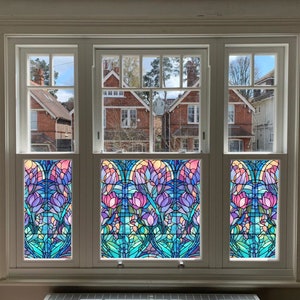 May include: A white window with three panes featuring stained glass panels. The stained glass panels depict a floral design with pink, purple, blue, and green colours.