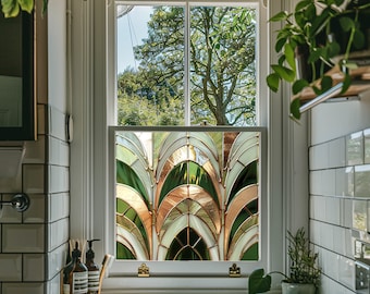 May include: A bathroom window with a stained glass window film featuring a geometric pattern of green, gold, and white arches. The window is framed in white and has a white window sill.