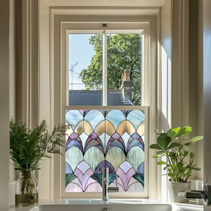 Könnte beinhalten: Ein Badezimmerfenster mit einer Buntglas-Fensterfolie mit einem geometrischen Muster aus überlappenden Bögen in Blautönen, Grün, Lila und Gold. Die Folie ist auf einem Einfachglasfenster mit weißem Rahmen angebracht.