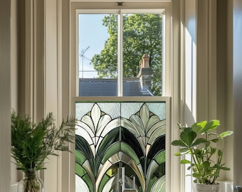 May include: A stained glass window featuring a geometric design in shades of green and white. The window is set in a white frame and is surrounded by a white wall. There are plants on either side of the window.
