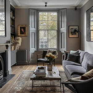 May include: A living room with a grey sofa, a black leather armchair, and a wooden coffee table with books on top. The room has a large window with grey shutters, a fireplace, and a bookshelf.