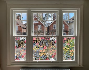May include: A window with three panes, each featuring a colorful floral design on the glass. The design includes flowers, leaves, and stems in shades of pink, yellow, blue, and green. The window looks out onto a row of brick houses.