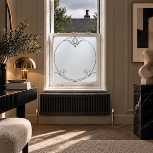 May include: A window pane featuring a frosted glass finish with a centred, dark-lined circular decorative motif. The design includes symmetrical, curved scrollwork at the top and bottom, creating an elegant, clean aesthetic within the frame.