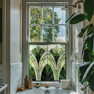 Peut inclure: Une salle de bain avec un mur carrelé blanc et une fenêtre avec un panneau de vitrail. Le panneau de vitrail présente un motif géométrique en verre vert et blanc. Il y a un lavabo en porcelaine blanche avec un robinet et une pomme de douche en arrière-plan.