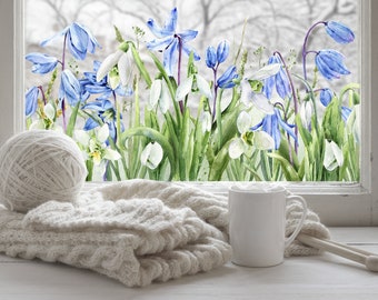 May include: A white ceramic mug sits on a white surface next to a ball of white yarn and a knitted sweater. A window behind the objects shows a watercolor painting of blue and white flowers.