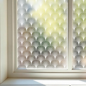 Könnte beinhalten: Fenster mit einer dekorativen Folie mit einem sich wiederholenden fächerförmigen Muster in Weiß. Das Design ist auf die Glasscheiben aufgebracht und erzeugt einen stilvollen und künstlerischen Look. Der Fensterrahmen ist weiß, und der Hintergrund zeigt einen Blick ins Freie.