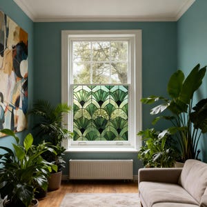 Puede incluir: Una ventana con una película decorativa de vidrieras con un patrón en forma de abanico en tonos verdes y negros. La ventana está en una habitación con paredes color turquesa, un sofá beige y varias plantas en macetas.