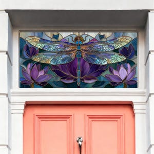 Könnte beinhalten: Ein Buntglasfenster mit einem Libellen-Design. Die Libelle ist in Blau-, Lila- und Goldtönen dargestellt und sitzt auf lila Lotusblumen. Das Fenster ist in Weiß gerahmt und befindet sich über einer korallenfarbenen Tür.