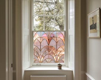 Può includere: Una finestra con un design in vetro colorato che presenta un motivo geometrico di archi rosa e dorati. La finestra è incorniciata in bianco ed è circondata da modanature bianche.