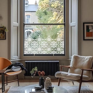 May include: A window with a decorative white floral pattern applied to the glass. The window is set in a black frame and is in a room with neutral-colored walls and wooden floors. The window treatment provides privacy while allowing light to pass through.