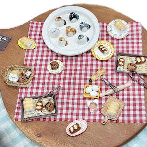 Peut inclure: Une collection de miniatures alimentaires et de figurines de chats en céramique disposées sur une surface à carreaux rouges et blancs. Comprend des assiettes de pâtisseries, un panier de pain et des ustensiles de boulangerie.