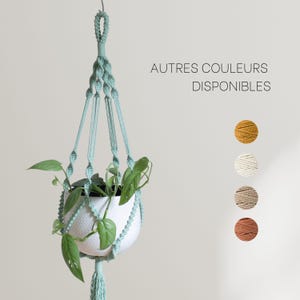 Peut inclure: Un porte-plante en macramé de couleur vert clair avec un pot blanc et une plante verte. Le texte "AUTRES COULEURS DISPONIBLES" est affiché à droite de l'image. Cinq échantillons de fil de différentes couleurs sont affichés sous le texte.
