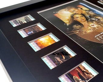 Könnte beinhalten: Ein gerahmtes Filmplakat für Star Wars Episode II: Angriff der Klonkrieger, mit einem schwarzen Rahmen und einem silbernen Passepartout. Das Plakat zeigt eine Szene aus dem Film mit Anakin Skywalker und Padmé Amidala. Der Rahmen enthält auch mehrere Filmzellenstreifen aus dem Film.