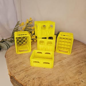 Könnte beinhalten: Fünf gelbe Plastikkisten, die auf einer Holzoberfläche gestapelt sind. Die Kisten haben ein Gittermuster und einige haben die Nummer "9V" aufgedruckt.