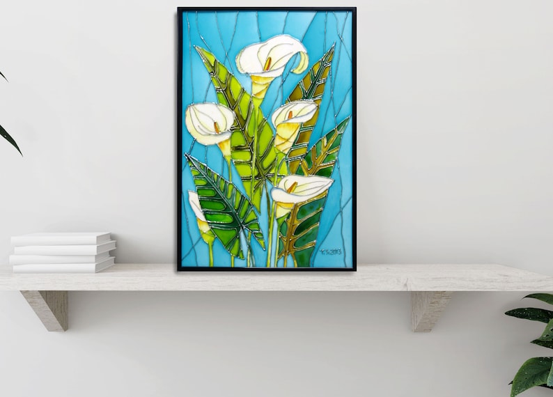 May include: A framed stained glass artwork featuring white calla lilies with green leaves on a blue background. The artwork is signed "T.C. 2013".