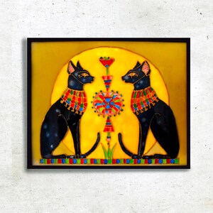 以下が含まれることがあります： 黄色い背景に、カラフルなディテールが施された黒い猫が2匹描かれた、額縁に入ったステンドグラスの芸術作品。猫たちは互いに向き合っており、間にスタイリッシュな花柄のデザインが施されています。