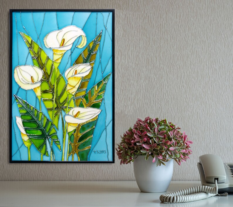 May include: A framed stained glass artwork depicting white calla lilies with green leaves on a blue background. The artwork is signed "Y.G. 2013".
