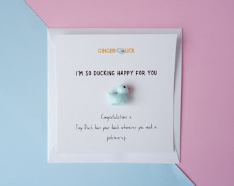 Puede incluir: Una tarjeta blanca con una figurita de pato azul claro pegada. La tarjeta dice "I'm so ducking happy for you" y "Congratulations x Tiny Duck has your back whenever you need a pick me up."