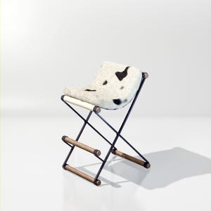 May include: A black metal folding stool with a wooden frame and a white and black cowhide seat.