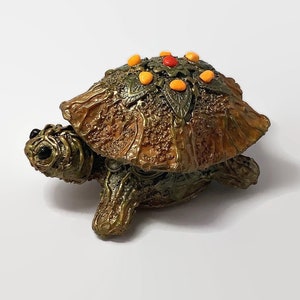 Könnte beinhalten: Eine kleine, dekorative Schildkrötenfigur mit einer detaillierten Schale. Die Schale ist braun und grün mit einer strukturierten Oberfläche und hat ein Muster aus orangefarbenen und roten Punkten. Die Schildkröte ist aus Harz und etwa 10 cm lang.