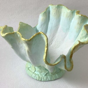 Peut inclure: Un pot en céramique bleu clair et doré avec un bord festonné et une base détaillée. Le pot est en forme de coquille.