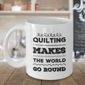 May include: White ceramic coffee mug with a black graphic that reads "Quilting makes the world go round".