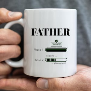 May include: White ceramic mug with the word "FATHER" in bold black letters. Below, a green progress bar graphic indicates "Phase 1 Completed" and "Phase 2 Loading... please wait."