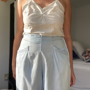 May include: A woman wearing a white tank top and light blue wide-leg pants with pockets.