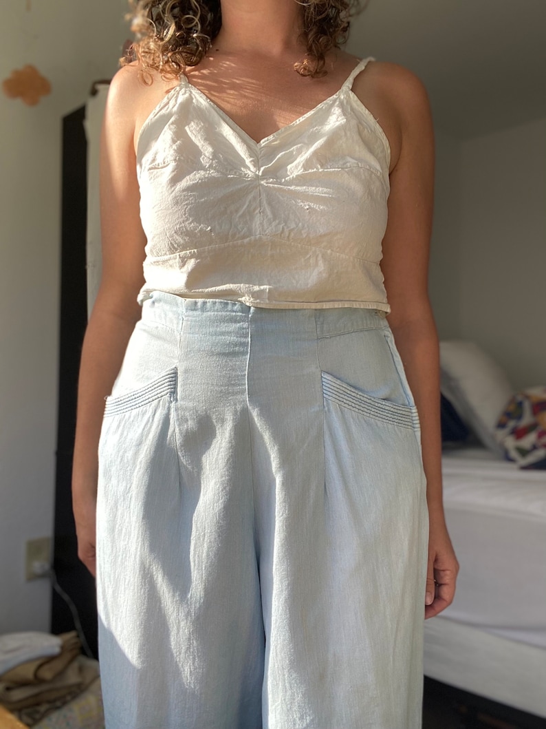 May include: A woman wearing a white tank top and light blue wide-leg pants with pockets.