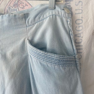 May include: Light blue denim pants with a single pocket on the right side. The pocket has a decorative stitching detail.