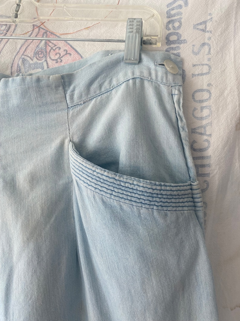 May include: Light blue denim pants with a single pocket on the right side. The pocket has a decorative stitching detail.