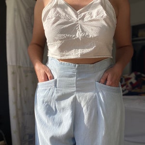 May include: A white cropped tank top with a v-neck and a pair of light blue high-waisted pants with pockets.