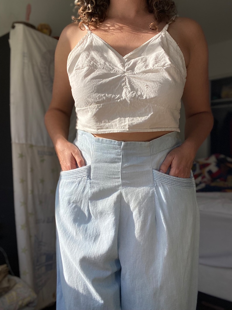 May include: A white cropped tank top with a v-neck and a pair of light blue high-waisted pants with pockets.