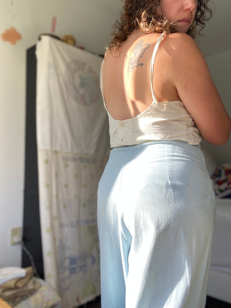 May include: A person wearing a white tank top and light blue wide-leg pants. The person has a tattoo on their back.